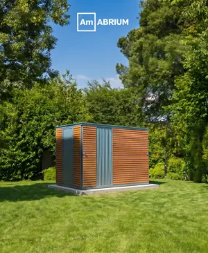 Small modern shed with wood slats and gray panels on a concrete pad in a sunny green backyard; ABRIM logo at the top.
