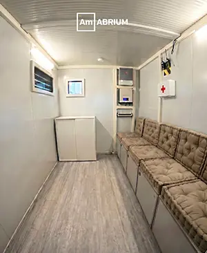 Interior of a mobile medical clinic: narrow corridor with beige cushioned benches along the right, white cabinets, and medical equipment at the far end.